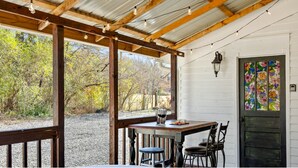 A covered outdoor seating area with a table, chairs, and a wine glass. - 1900 Farmhouse with Luxury Spa Bath, 2 Master Bedrooms, Historic Home (Whitwell)