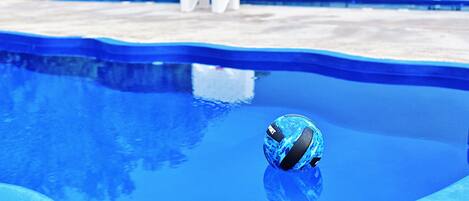 A swimming pool with a blue ball, white lounge chairs, and a white chair in the background.