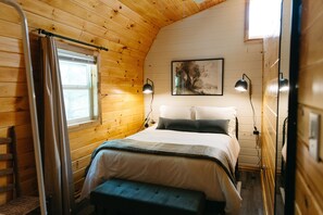 Ein gemütliches Schlafzimmer in einer Holzh ütte mit Bett, Bank und einem Gemälde an der Wand.