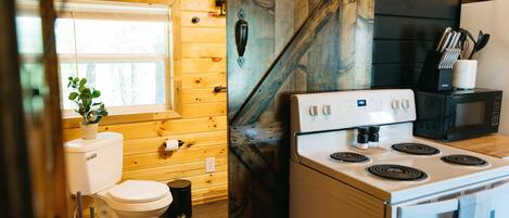 Une cuisine de taille réduite, équipée d’une cuisinière, d’un four à micro-ondes et dotée de murs en bois.