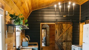 A rustic kitchen with wooden walls and a sloped ceiling, featuring a bar area with stools, a sink, and a stove. - Lumber Lodge RRG - COMFY WOODSY STAY - in RRG/Auxier (Pine Ridge)