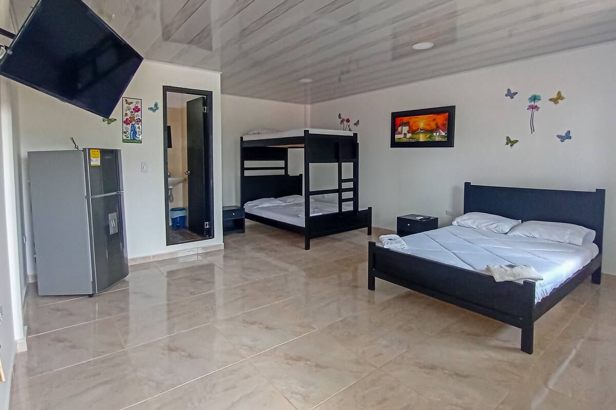 Une chambre comprenant un lit superposé, un lit simple, un téléviseur à écran plat, un réfrigérateur et un évier.