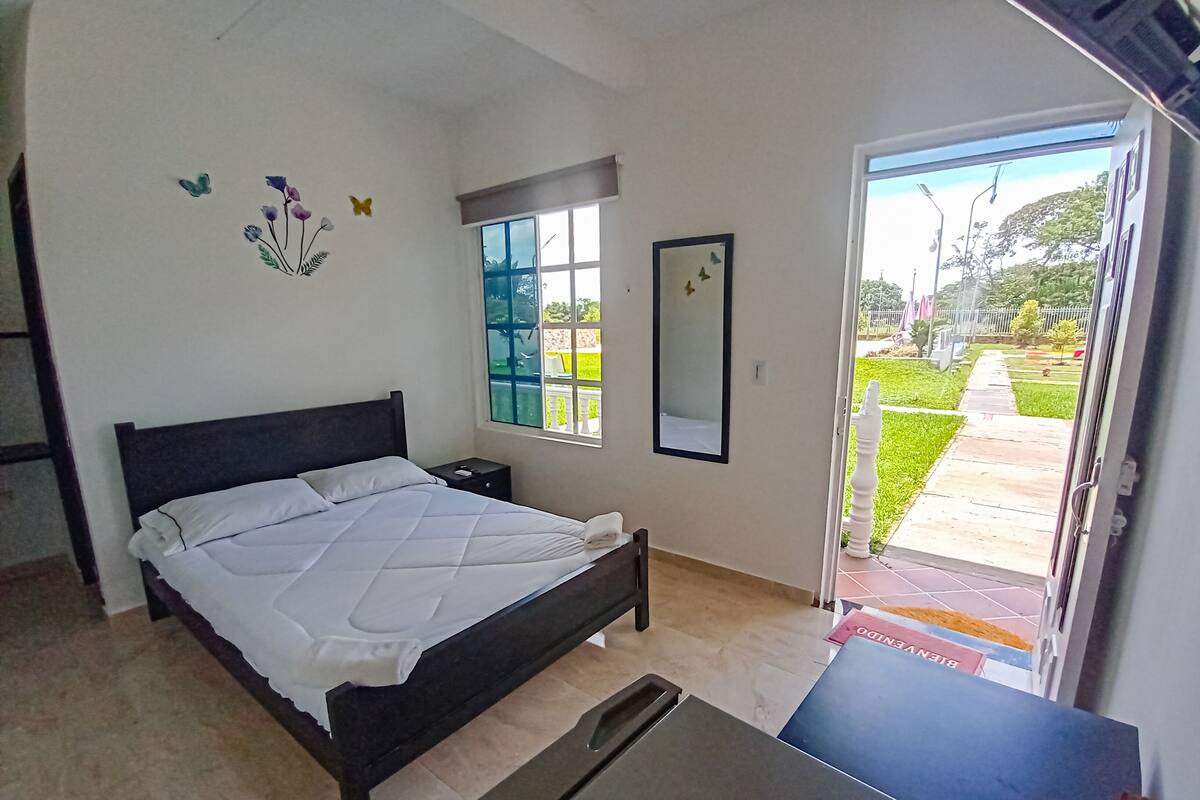 Une chambre à coucher avec un lit, une table de chevet, une fenêtre, un miroir et une vue sur l’extérieur.