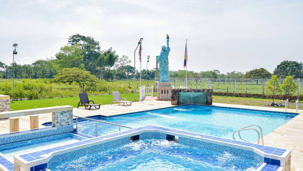 A swimming pool with a statue, surrounded by a fence and greenery. - Hotel Cabañas American Dream (Restrepo)