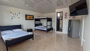 A bedroom with a bed, a nightstand, a wall-mounted TV, a refrigerator, and a bathroom visible through an open door. - Hotel Cabañas American Dream (Restrepo)