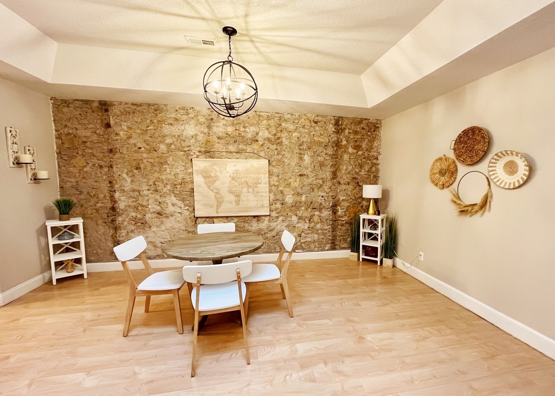 Un comedor con una mesa redonda y cuatro sillas, una pared de piedra, un mapa mundial y objetos decorativos en la pared.