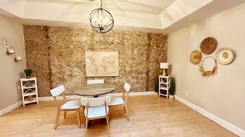 Un comedor con una mesa redonda y cuatro sillas, una pared de piedra, un mapa mundial y objetos decorativos en la pared.