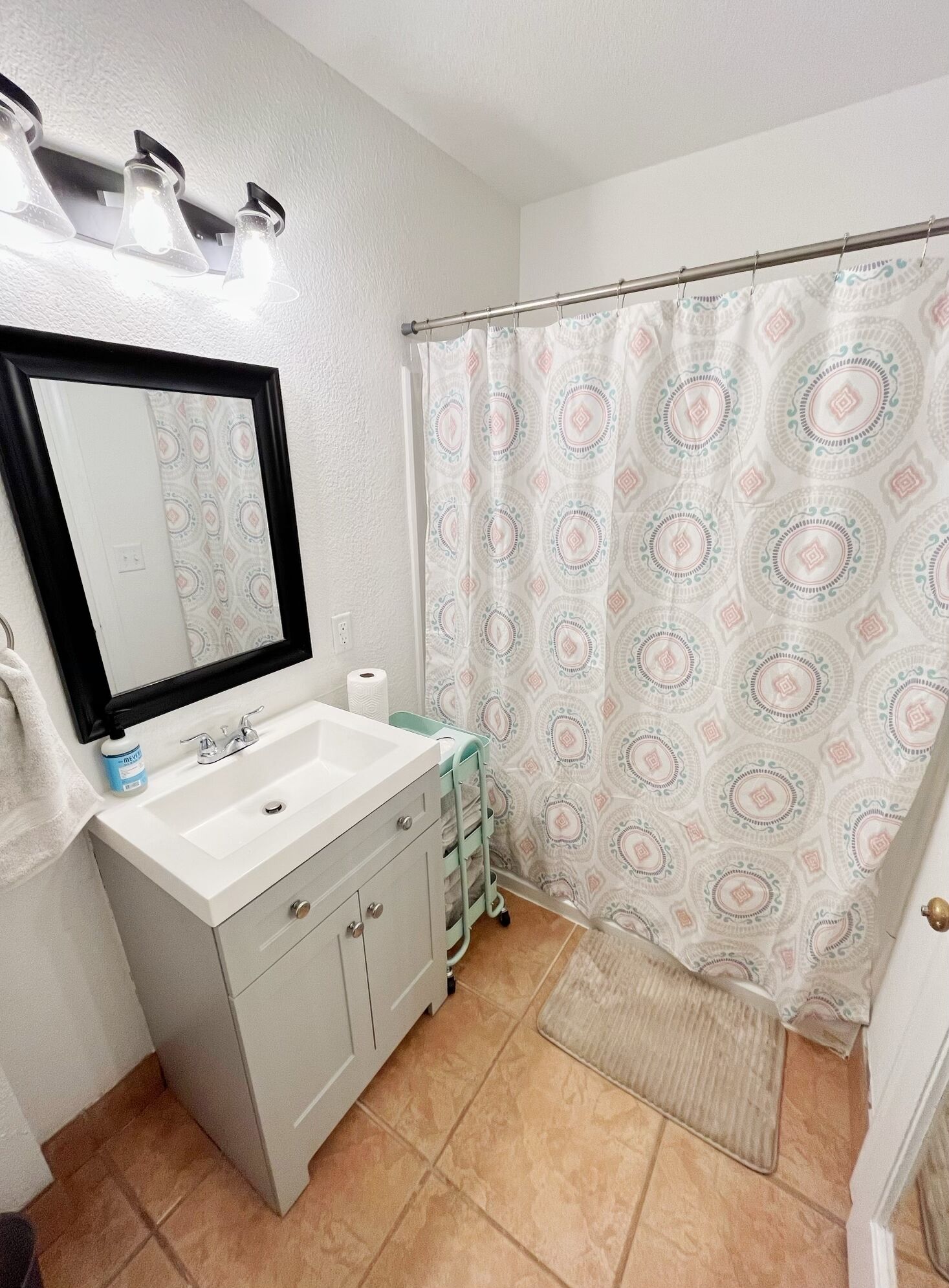 A bathroom with a white sink, a mirror, a towel, a shower curtain, and a small rug.