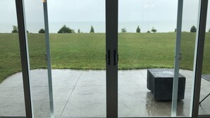 Udsigt gennem en glasdør med en beton terrasse og en græsmark i baggrunden.