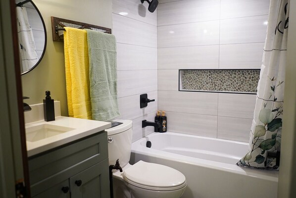 Un baño con inodoro, lavabo y bañera. Hay dos toallas colgadas en un perchero.