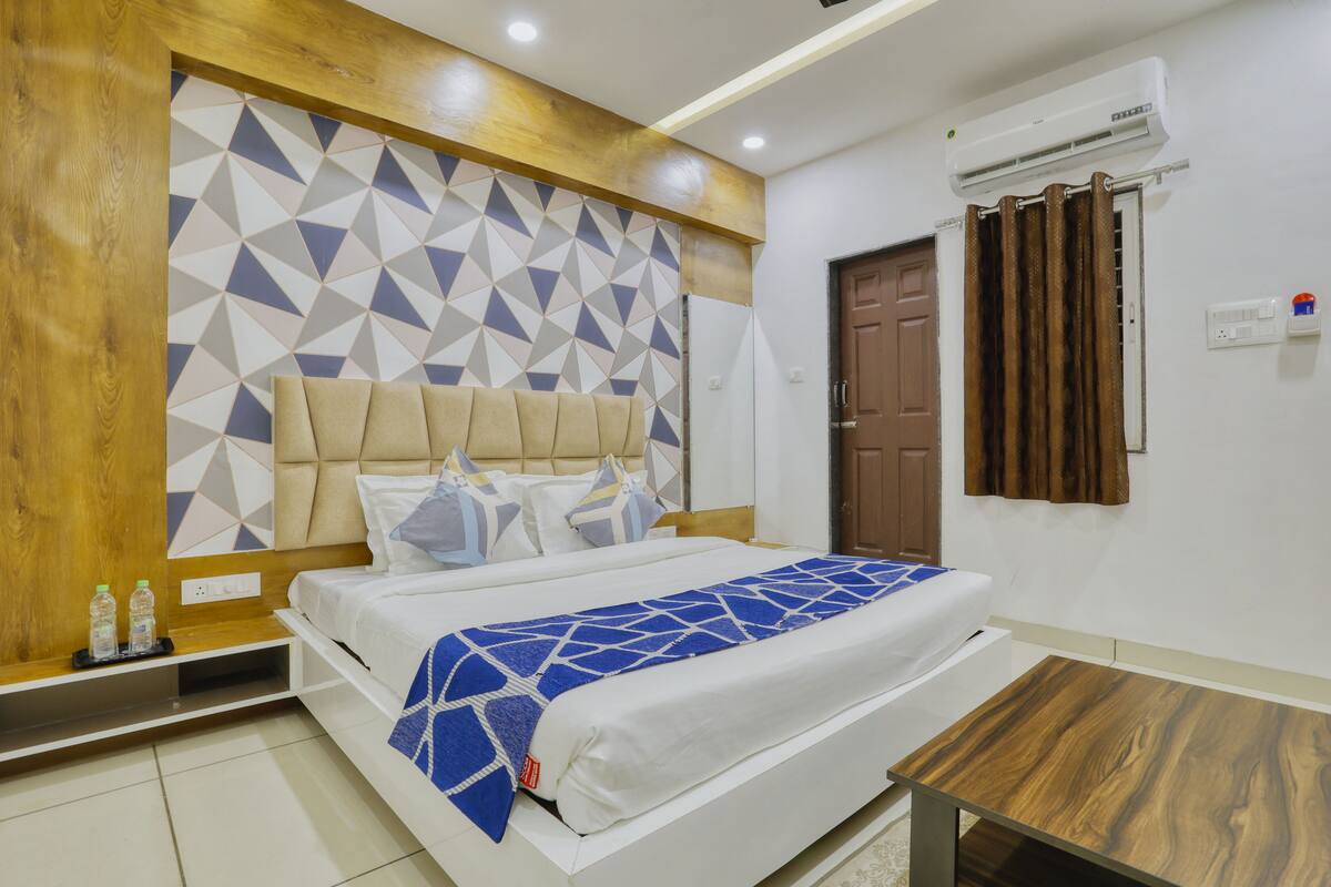 A hotel room with a bed, a wooden headboard, a geometric-patterned wall, an air conditioning unit, and a wooden table.