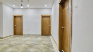 Un couloir avec deux portes en bois, un luminaire et un sol carrelé.