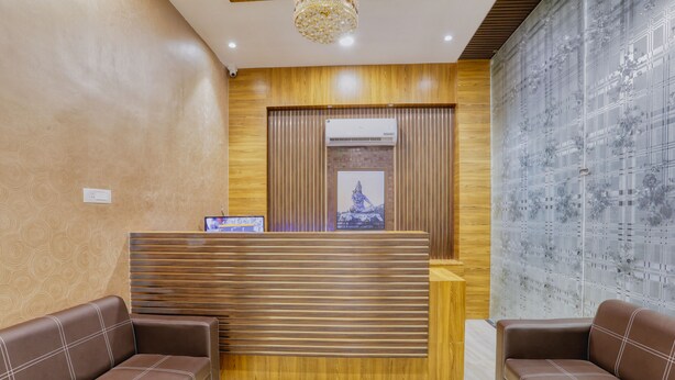 Un espace d’accueil avec un comptoir de réception en bois, deux canapés marron et un mur orné d’un motif.