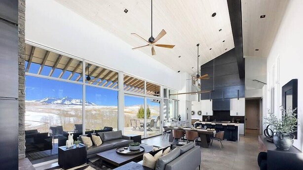 A spacious living area with a large window overlooking a mountainous landscape, a modern kitchen, and a dining area with a high ceiling and ceiling fans. - Telluride Luxe: Style and Space 3 mins to Skiing! (Mountain Village)