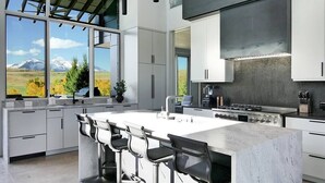A modern kitchen with a large island, bar stools, and a view of mountains. - Telluride Luxe: Style and Space 3 mins to Skiing! (Mountain Village)