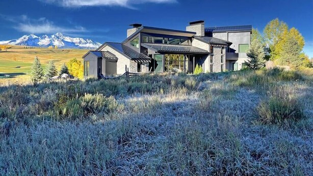 A modern house with a large glass facade, surrounded by a mountainous landscape and a clear sky. - Telluride Luxe: Style and Space 3 mins to Skiing! (Mountain Village)