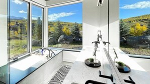 A modern bathroom with large windows, a bathtub, a sink, and a mirror. - Telluride Luxe: Style and Space 3 mins to Skiing! (Mountain Village)