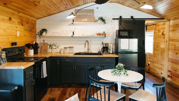 Une cuisine avec des murs en bois, un îlot central, des meubles de couleur noire et un plan de travail blanc.