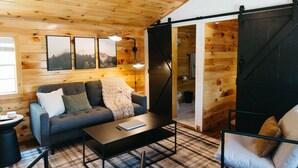 L’intérieur chaleureux d’un chalet avec un plafond en bois, un canapé, une table basse et une porte coulissante.