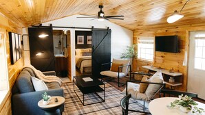 L’intérieur chaleureux d’un chalet comprend un canapé, des fauteuils, une table à manger, un ventilateur de plafond et un téléviseur fixé au mur.