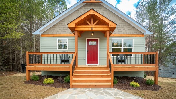 Une maison à deux étages avec une porte d’entrée rouge, un porche en bois et un chemin de pierre menant à l’entrée.