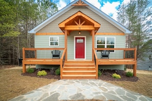 A two-story house with a red front door, wooden front porch, and a stone pathway leading to the entrance.