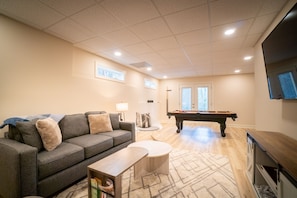 A living room with a sofa, coffee table, and a pool table.