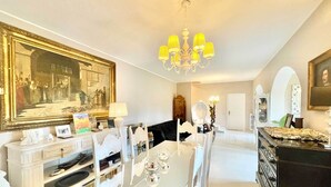 A dining area with a white table, chairs, and a chandelier. There is a large framed painting on the wall and a mirror above the table. - Villa Alice, Menaggio, Italy (Menaggio)