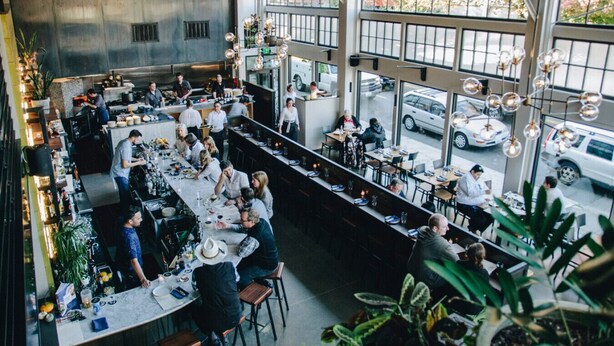 Un restaurant spacieux avec de hauts plafonds, de grandes fenêtres et un design moderne de style industriel.