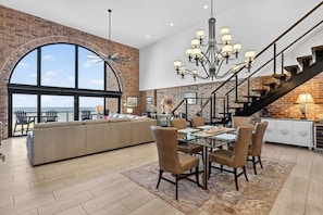 A spacious living room with a large window, a dining area with a glass table, and a staircase with a view.