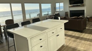 A spacious living area with a large white island, a brown leather sofa, and a fireplace. - Oceanfront Cayucos Cottage on the sand (Cayucos)