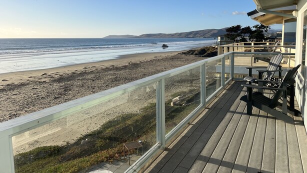 A wooden deck with a glass railing overlooking a beach. - Oceanfront Cayucos Cottage on the sand (Cayucos)