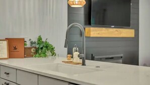 Une cuisine moderne avec un plan de travail blanc, un robinet en acier inoxydable, un porte-savon en bois et un luminaire suspendu.