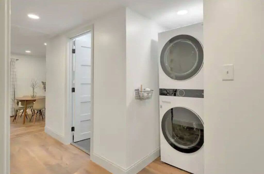 Una sala de bugaderia amb dues rentadores, una porta que condueix a una altra habitació i una taula petita amb cadiretes.
