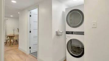 Una sala de bugaderia amb dues rentadores, una porta que condueix a una altra habitació i una taula petita amb cadiretes.