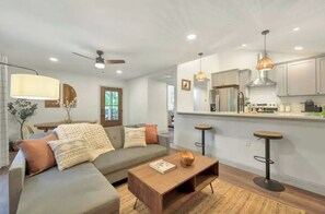 Relax in this inviting living area with a comfortable sofa, coffee table, and bar stool, surrounded by modern kitchen amenities.
