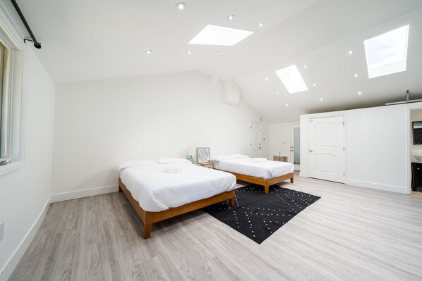 A modern bedroom with two beds, a skylight, and a wardrobe.