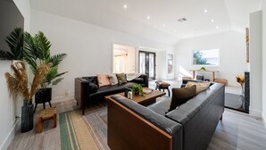 A spacious living room with a black leather sofa, a wooden coffee table, and a large potted plant. - Brentwood Pool/Spa Home Close to Everything! (Los Angeles)