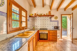 A kitchen with a double sink, a stove, a microwave, wooden cabinets, and a window with a view of greenery. - Villa Navarro with swimming pool in Pollensa (Pollensa)
