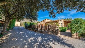 A stone house with a gravel driveway, surrounded by trees and greenery. - Villa Navarro with swimming pool in Pollensa (Pollensa)