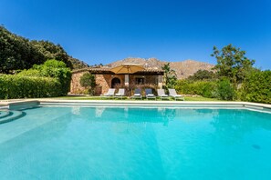 A pool with lounge chairs and a stone building with arches.