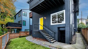 A modern two-story house with a visible staircase leading to the second floor, a small deck, and a well-maintained lawn. - Lovely condo overlooking the Fremont Bridge (Seattle)