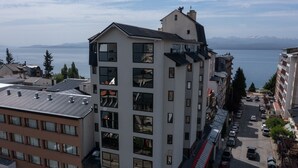 A multi-story hotel with a view of a lake and mountains in the background. - American Suites (San Carlos de Bariloche)