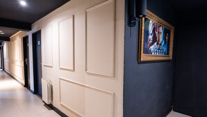 A hotel corridor with cream-colored walls, a radiator, and a framed movie poster on the right wall. - American Suites (San Carlos de Bariloche)