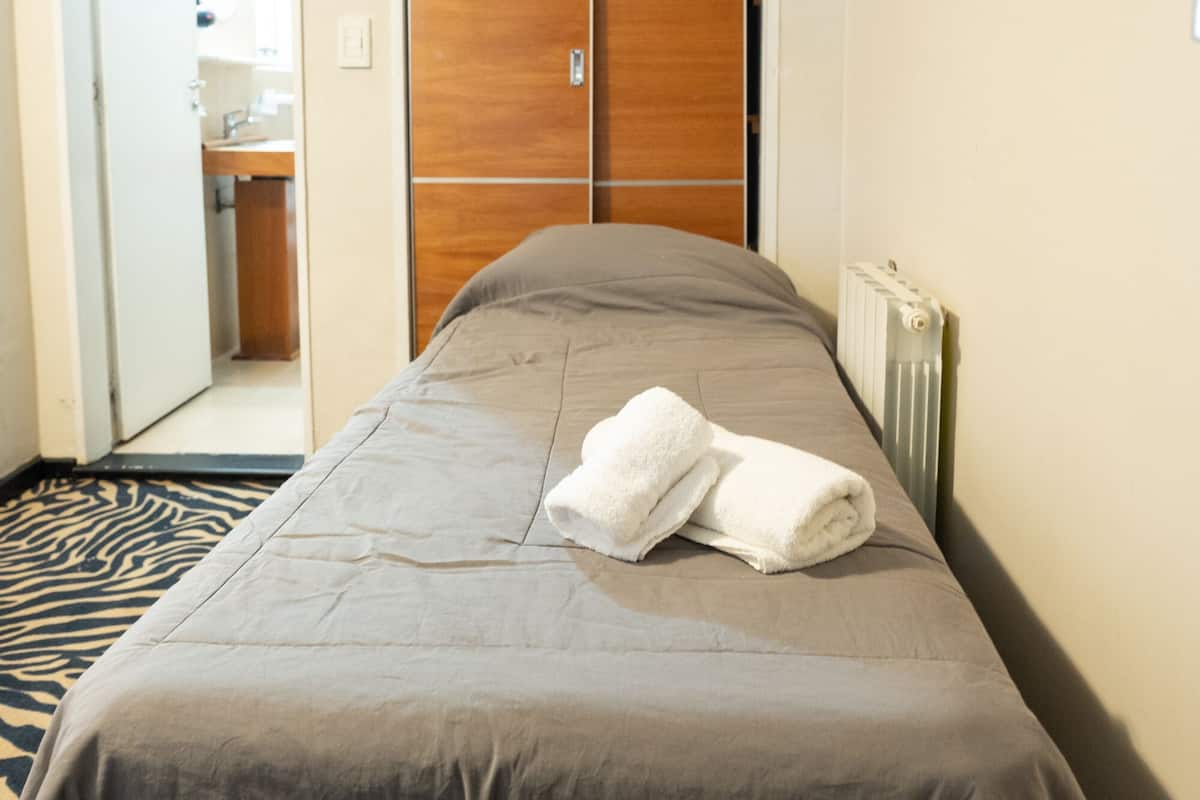 Habitación de hotel con cama, televisor montado en la pared y armario.