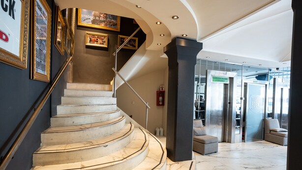 A marble staircase with a handrail, leading to a lobby area with a glass door entrance and a seating area. - American Suites (San Carlos de Bariloche)