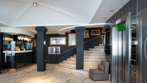 A lobby with a marble floor, a staircase, a reception desk, and framed pictures on the wall. - American Suites (San Carlos de Bariloche)