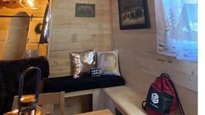 Un interior de cabaña acogedor, con paredes de madera, un banco, una mesa y una ventana con vistas.