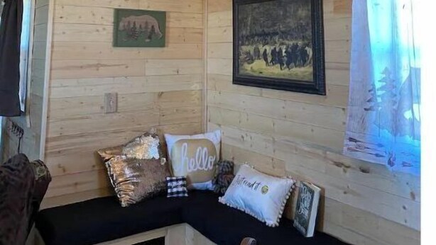Interior acogedor de una cabaña con paredes de madera, un banco con almohadones y un cuadro en la pared.