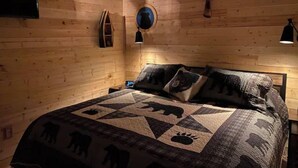 Un dormitorio de cabaña de madera con una cama, un reloj de pared y una lámpara fijada.